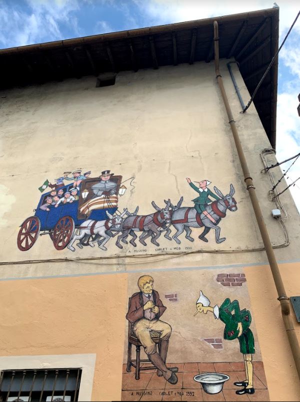 murales a Vernante della carrozza verso il Paese dei Balocchi con Pinocchio e murales in basso con Geppetto